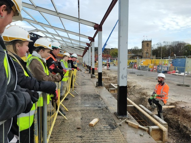 students at construction site with PPE listening to construction worker talk